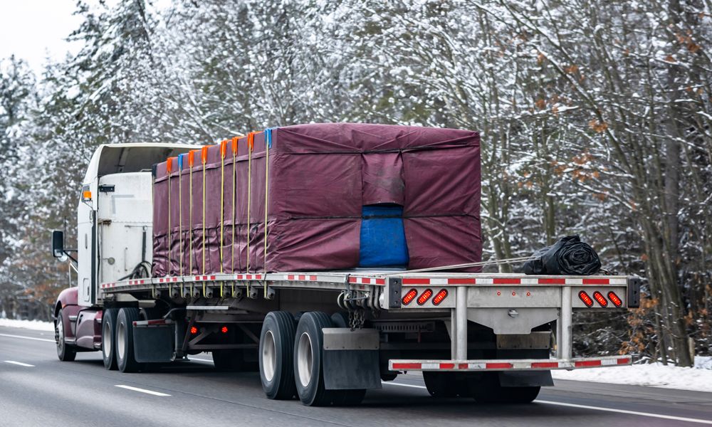flatbed trailer with tarp, edge protectors driving through snowy landscape