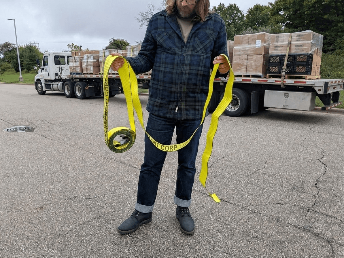 man holding winch strap in front of flatbed trailer